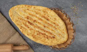 Chlebek naan w koszyku, obok wałek i ziarna pszenicy.