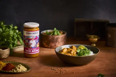 Słoik sosu Tikka Masala i miska z daniem z ryżem, kurczakiem i kolendrą.