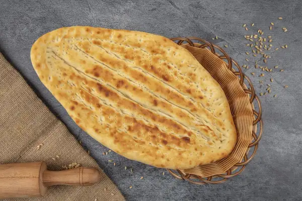 Chlebek naan w koszyku, obok wałek i ziarna pszenicy.